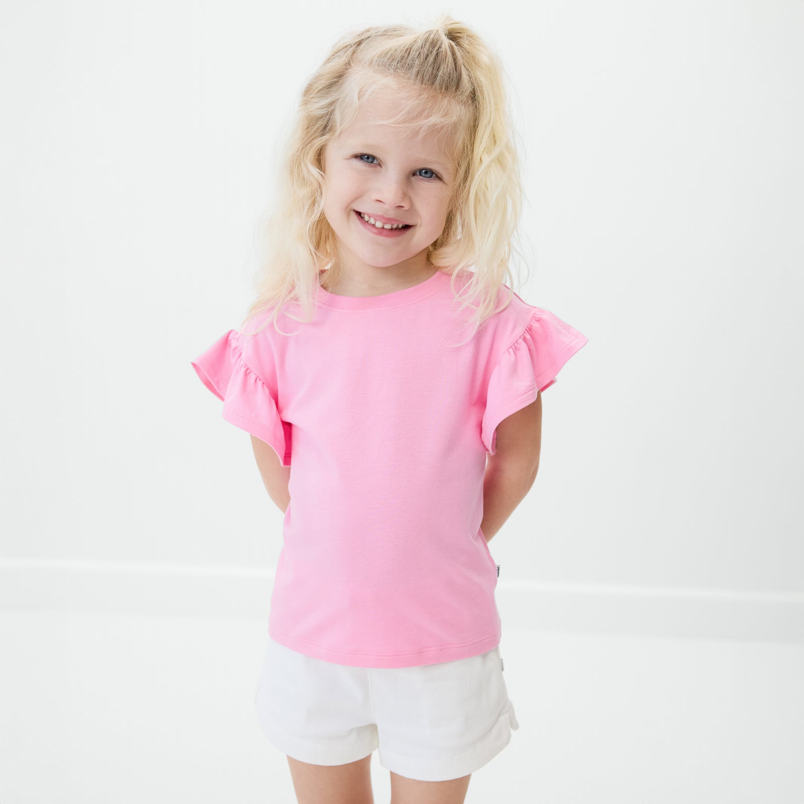 Standing child wearing the Peppy Pink Ruffle Tee with bright white denim shorts