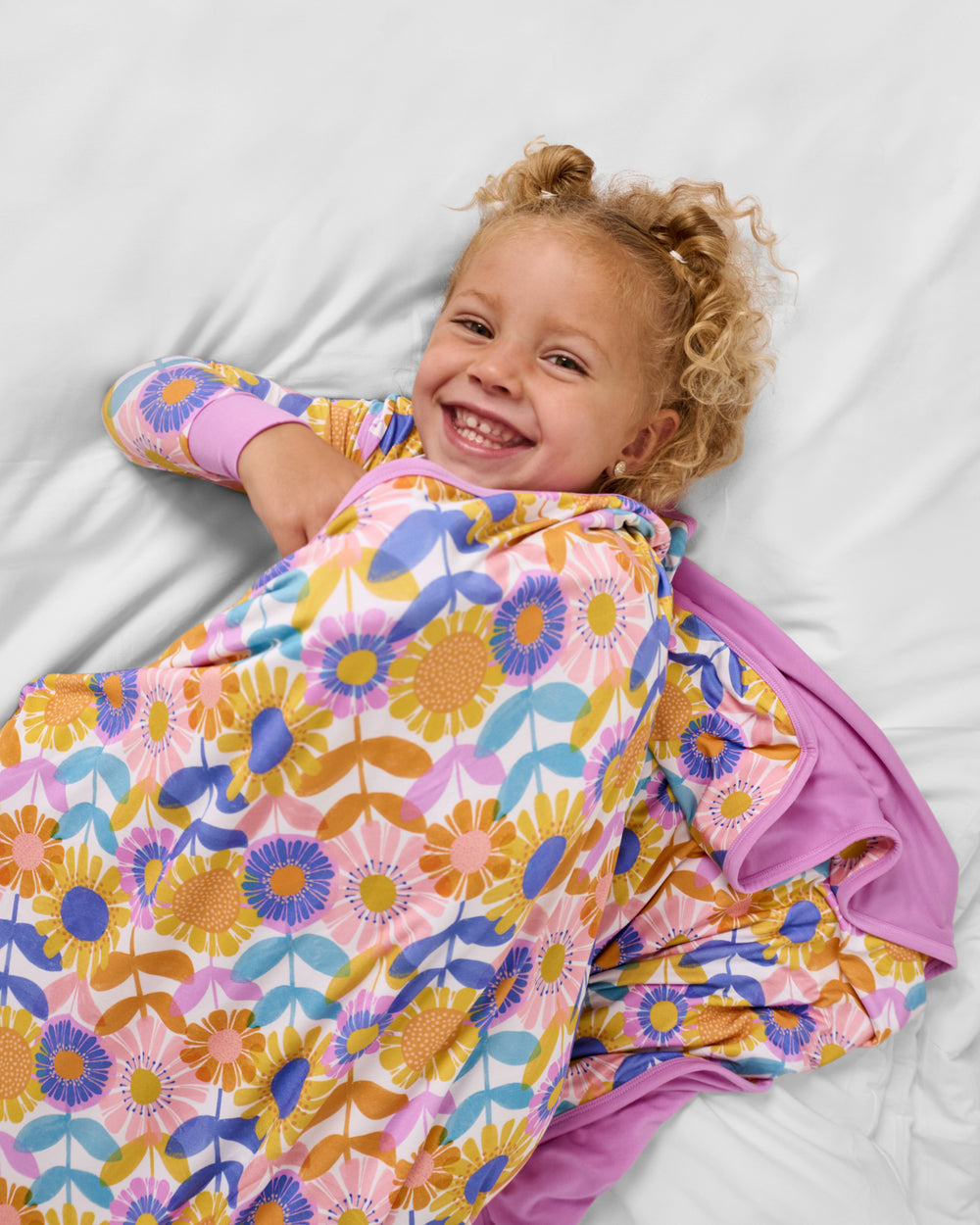 Girl wrapped in the Petal Power Large Cloud Blanket® on a white bed