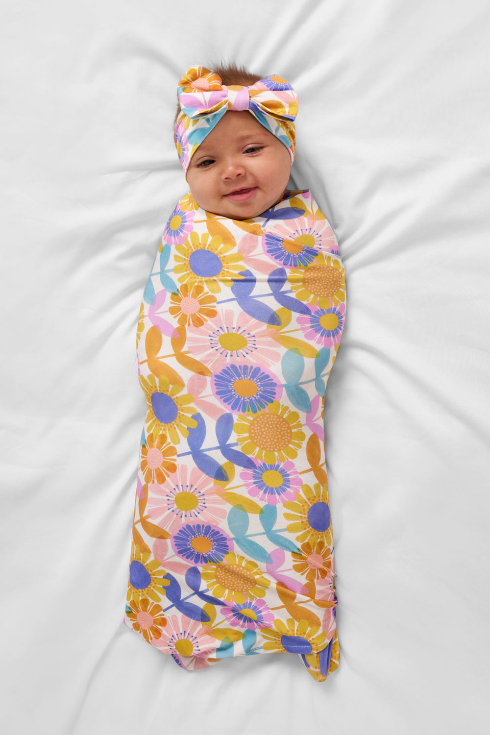 Aerial view of baby wearing the Petal Power Swaddle & Luxe Bow Headband Set