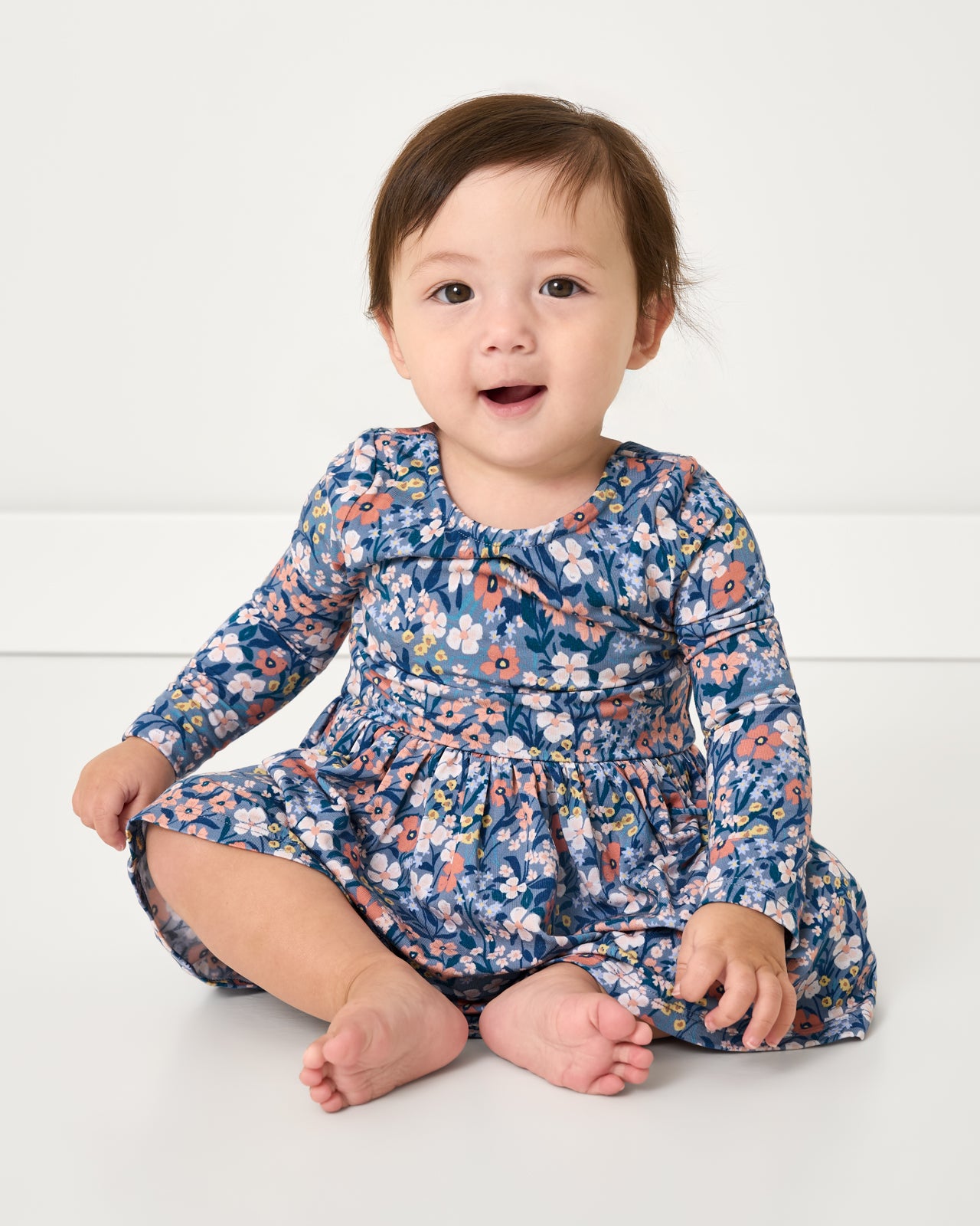Sitting baby wearing the Petite Petals Bow Back Skater Dress with Bodysuit