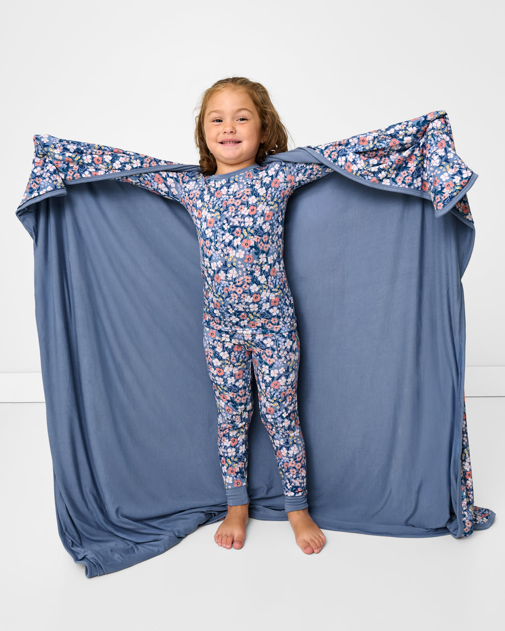 Standing girl holding up the Petite Petals Large Cloud Blanket® showing the solid blue side