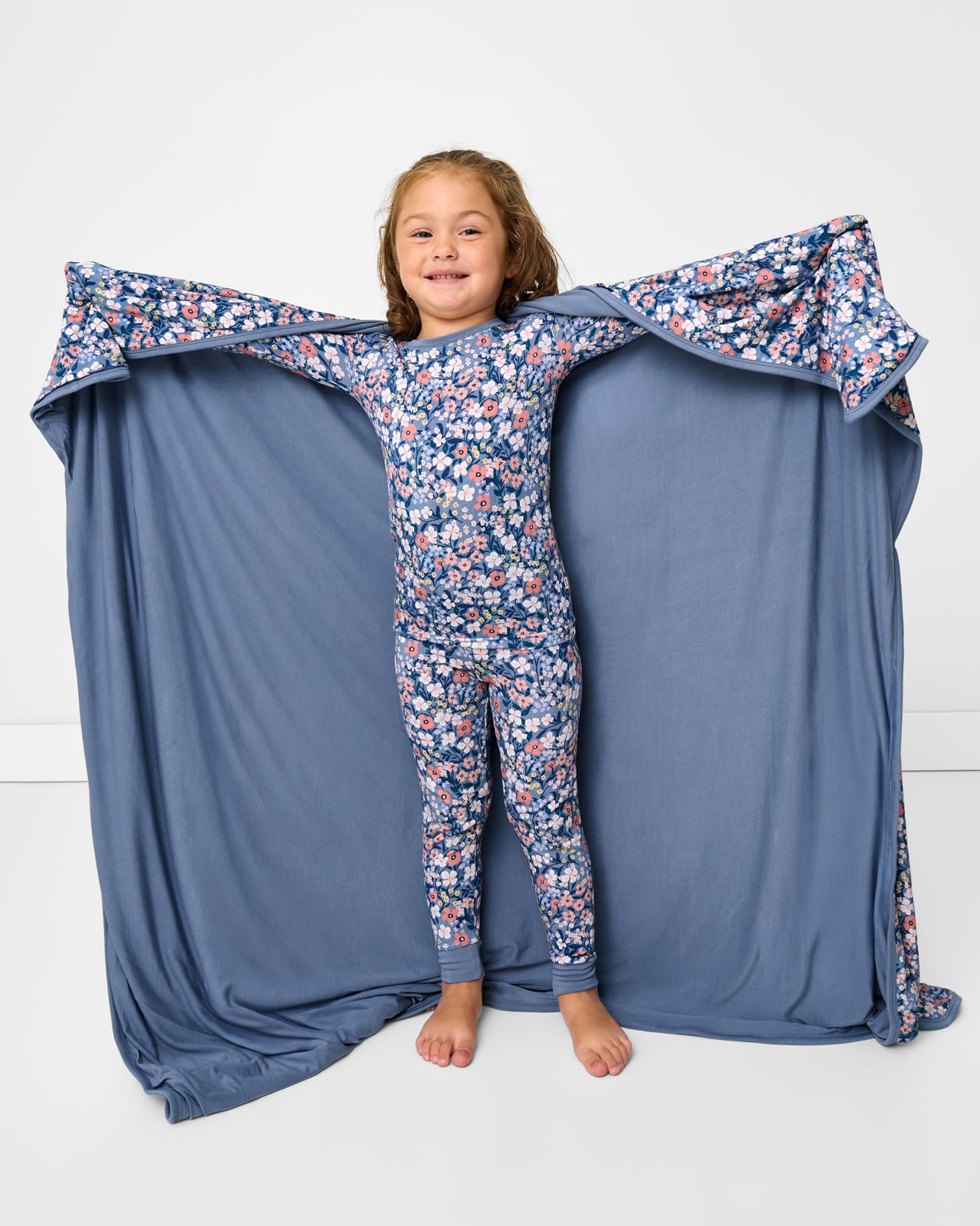 Standing girl holding up the Petite Petals Large Cloud Blanket® showing the solid blue side