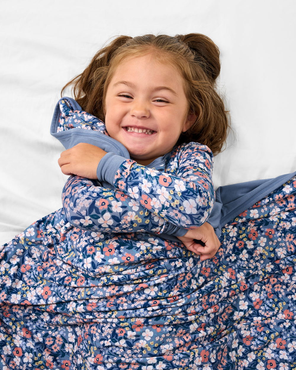 Girl snuggled with the Petite Petals Large Cloud Blanket® on a white bed