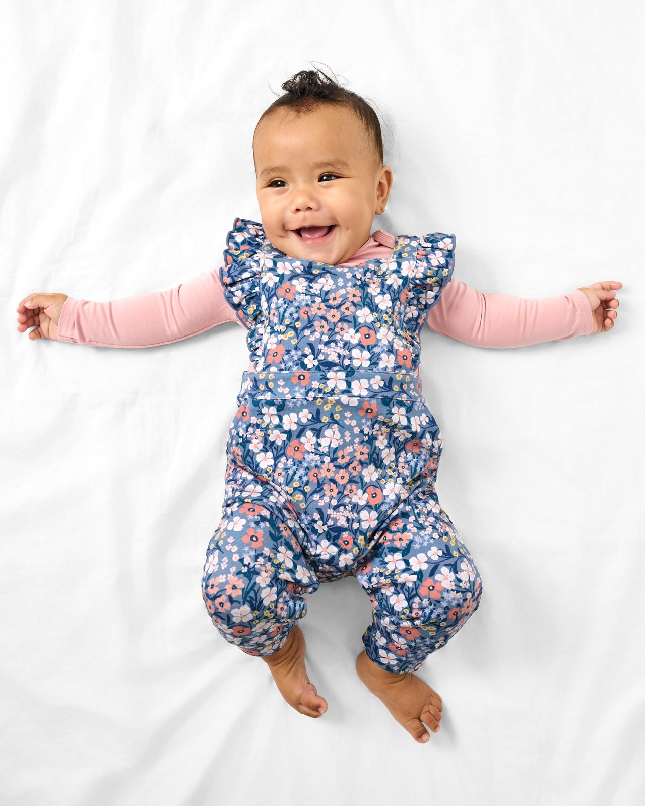 Aerial view of baby wearing the Petite Petals Ruffle Overall with a pink bodysuit