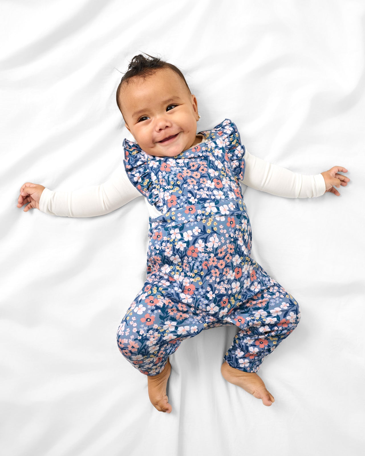 Aerial view of baby wearing the Petite Petals Ruffle Overall over a white long sleeve bodysuit