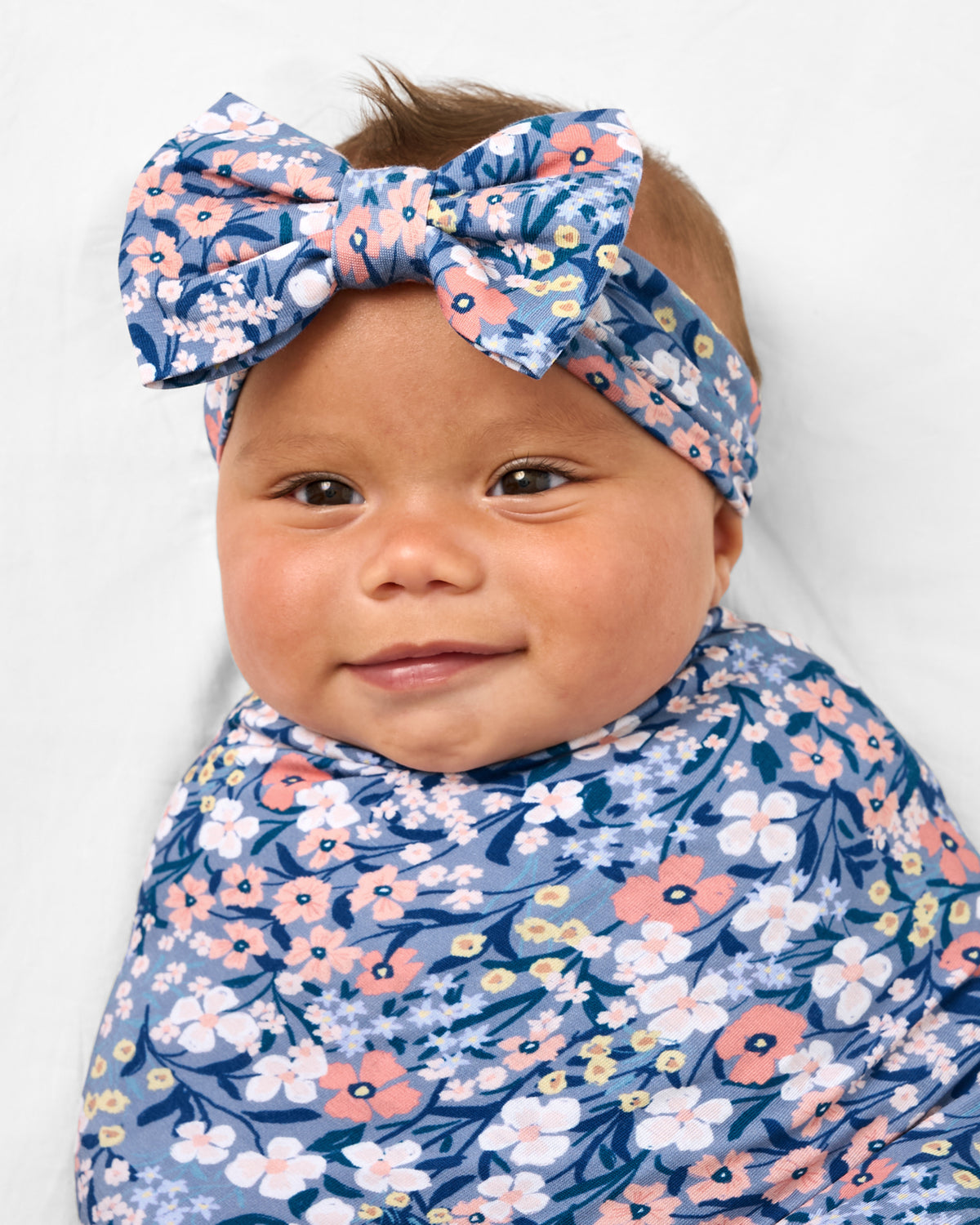 Close up of baby wearing the Petite Petals Swaddle & Luxe Bow Headband Set