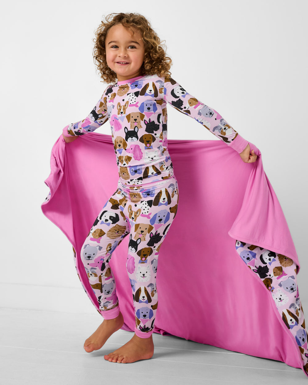 Girl wearing the Puppy Parade PJs holding the Pink Puppy Parade Large Cloud Blanket® 