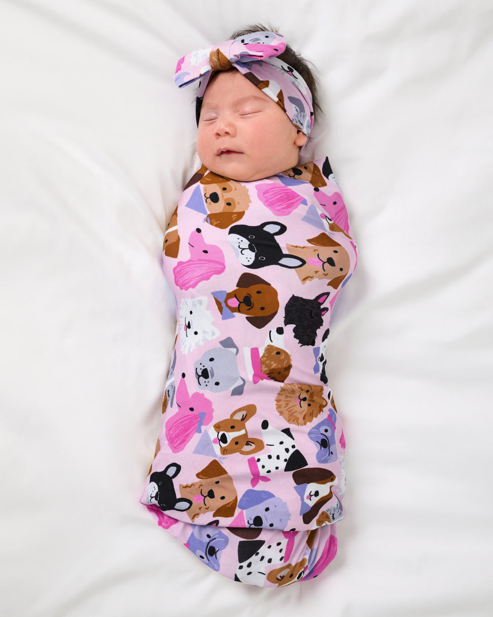 Aerial view of baby wearing the Pink Puppy Parade Swaddle & Luxe Bow Headband Set