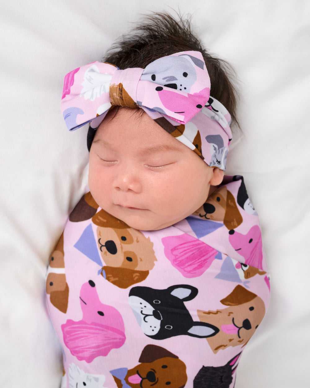 Close up of baby wearing the Pink Puppy Parade Swaddle & Luxe Bow Headband Set