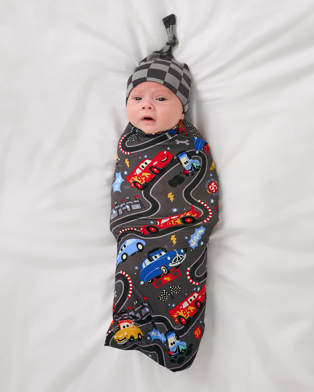 Aerial view of baby wearing the Disney & Pixar Piston Cup Swaddle & Hat Set