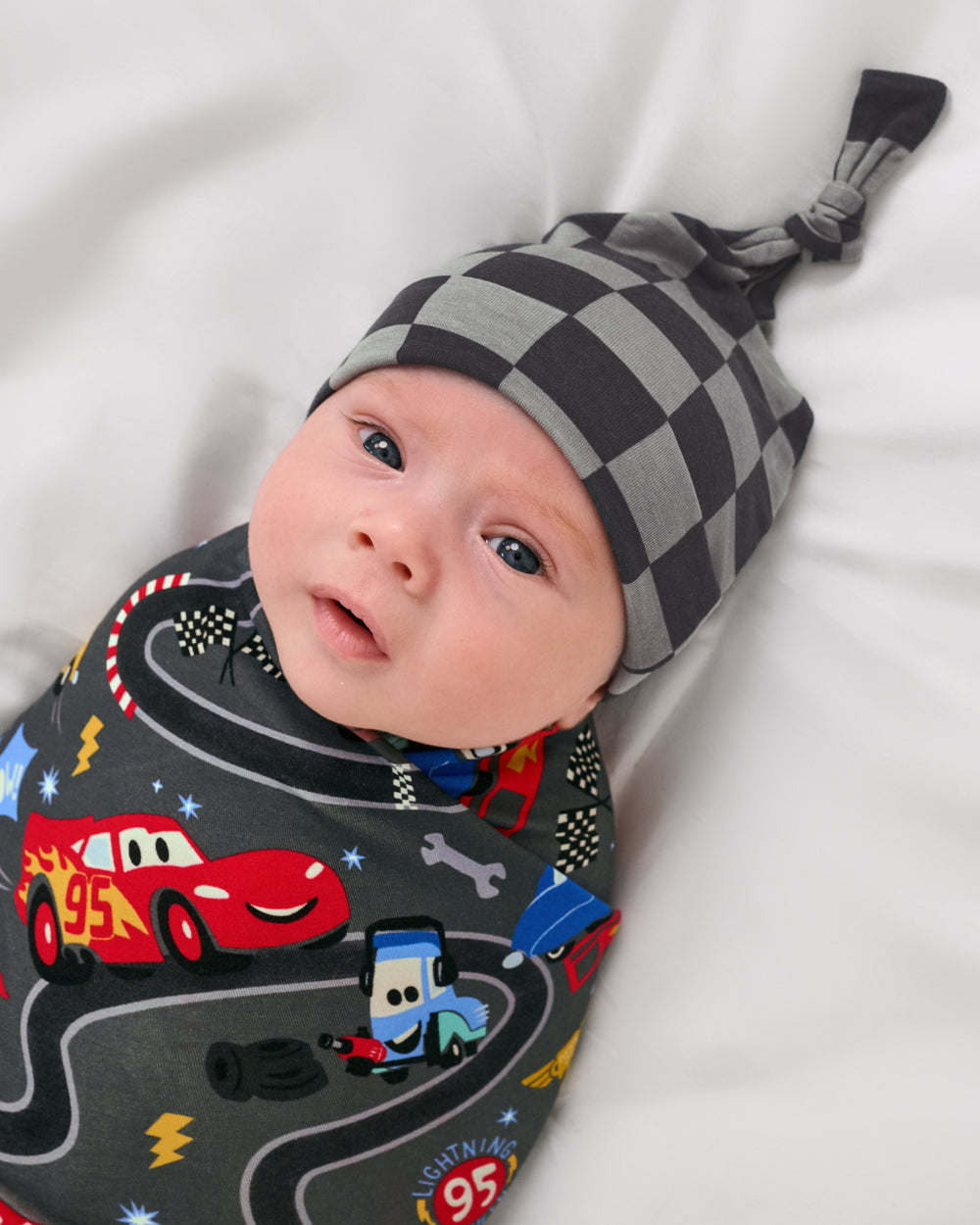 Close up of baby wearing the Disney & Pixar Piston Cup Swaddle & Hat Set