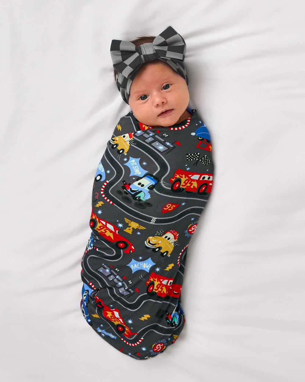 Aerial view of baby wearing the Disney & Pixar Piston Cup Swaddle & Luxe Bow Headband Set