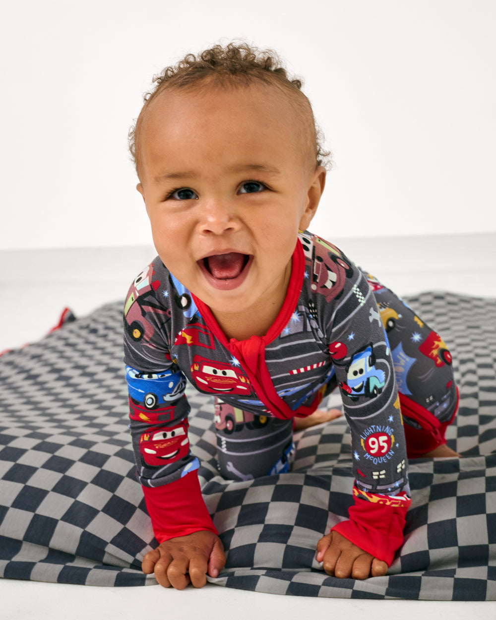 Child wearing the Disney & Pixar Piston Cup Zippy crawling on the checkered print blanket