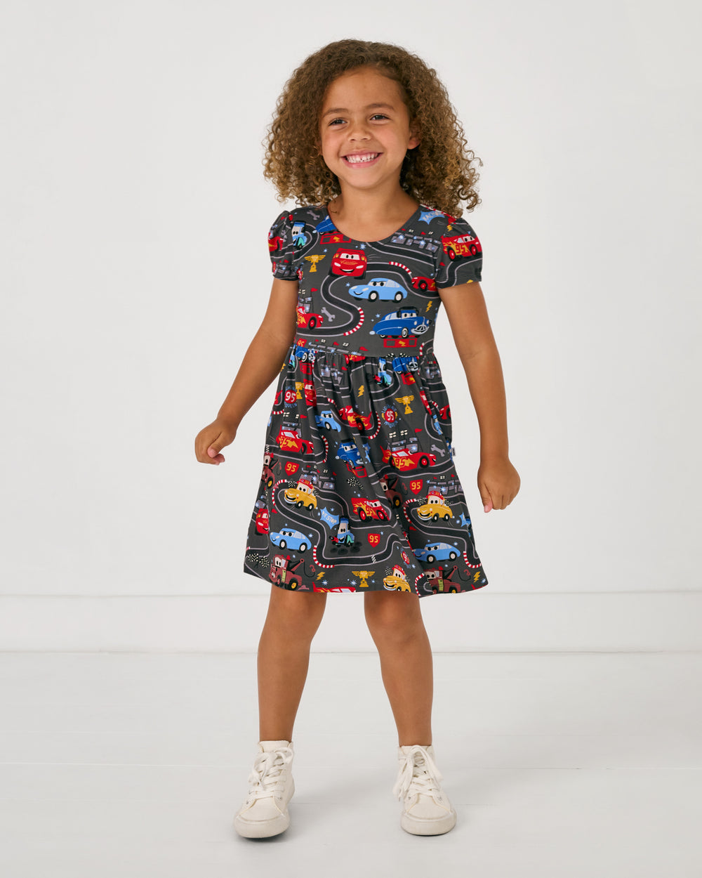 Standing girl wearing the Disney & Pixar Piston Cup Bow Back Skater Dress