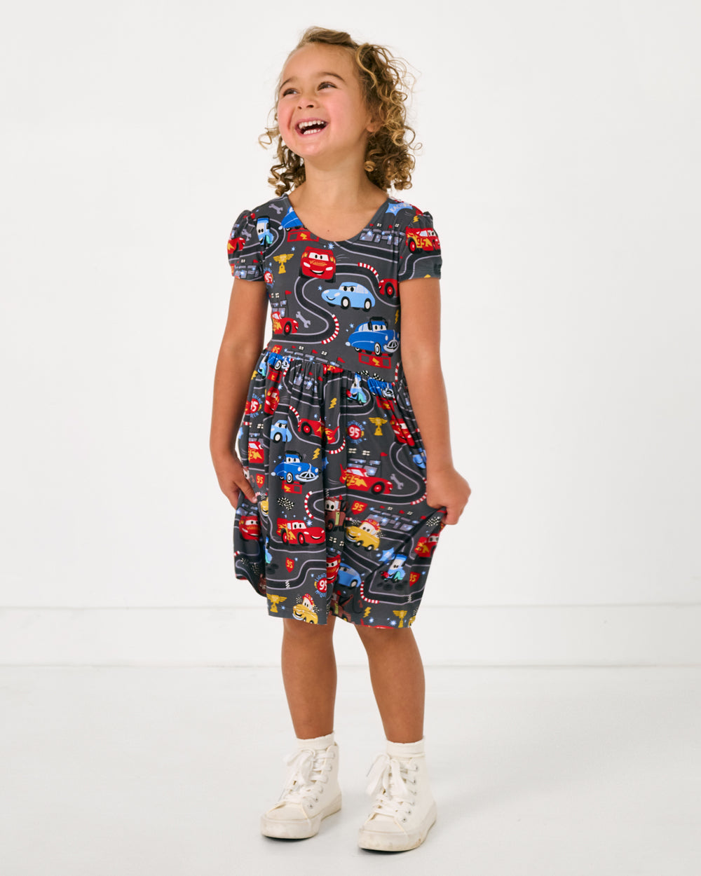 Girl wearing the Pixar Cars Piston Cup Bow Back Skater Dress on a white background