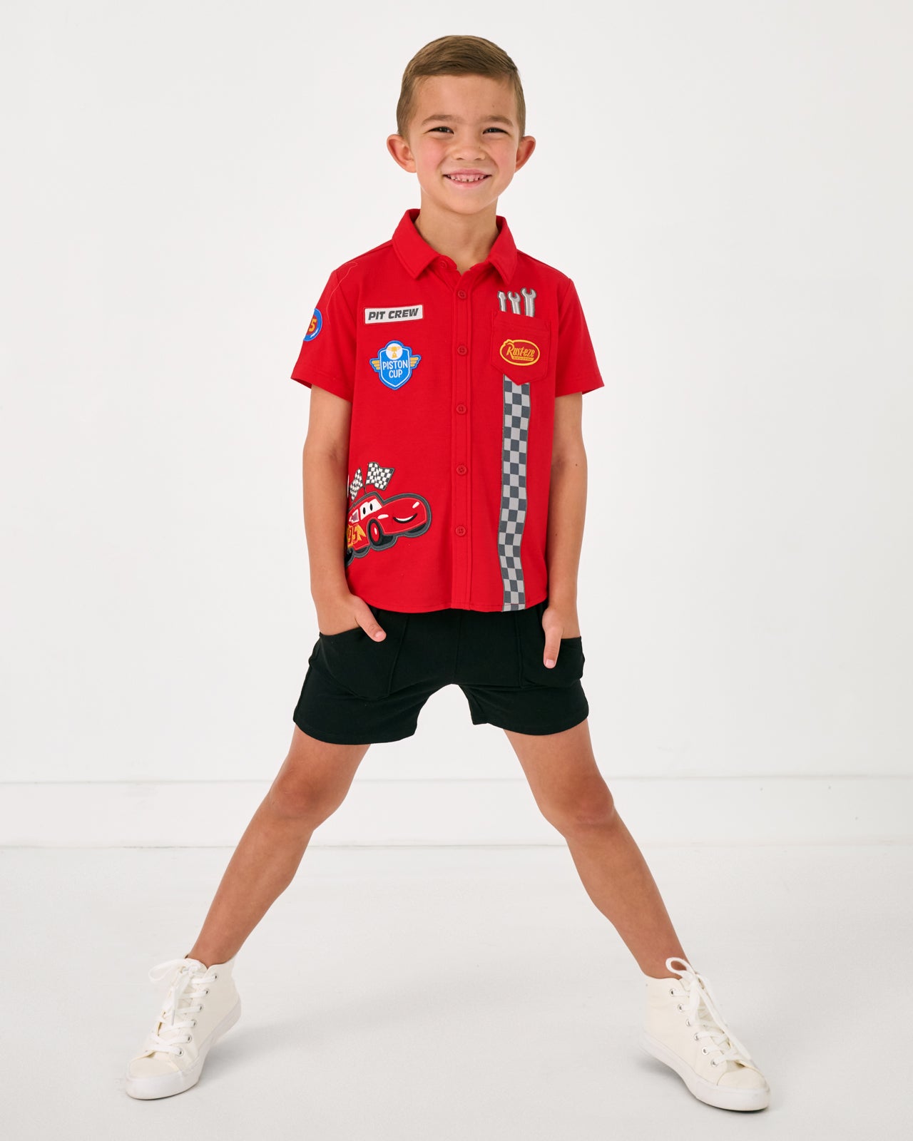 Standing boy wearing the Disney & Pixar Piston Cup Button Down Polo and black boys shorts