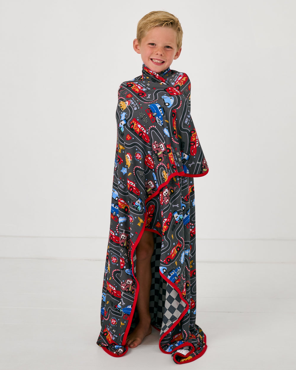 Boy wrapped in the Disney & Pixar Piston Cup Large Cloud Blanket®
