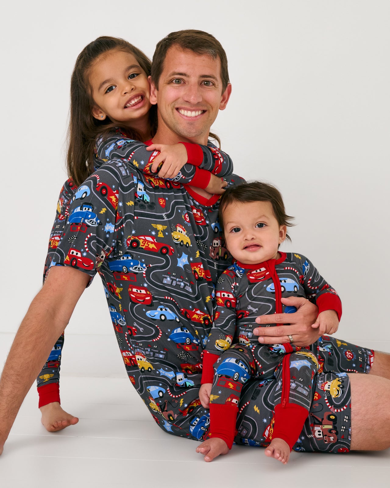 Father and two children wearing matching Pixar Cars Piston Cup pajamas