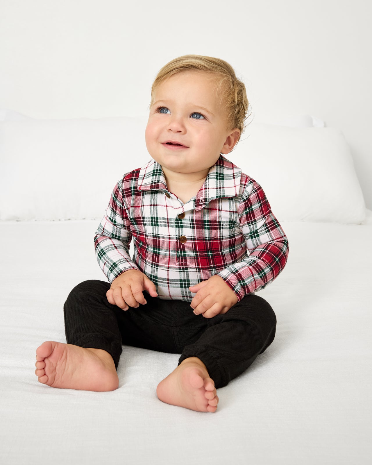 Sitting baby wearing the Holly Plaid Polo Bodysuit with black pants