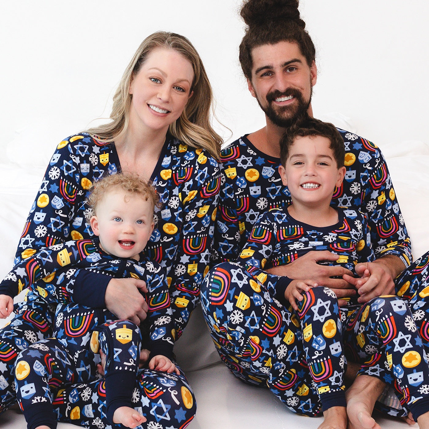 Family of four sitting on the ground wearing matching Playful Dreidels pajamas