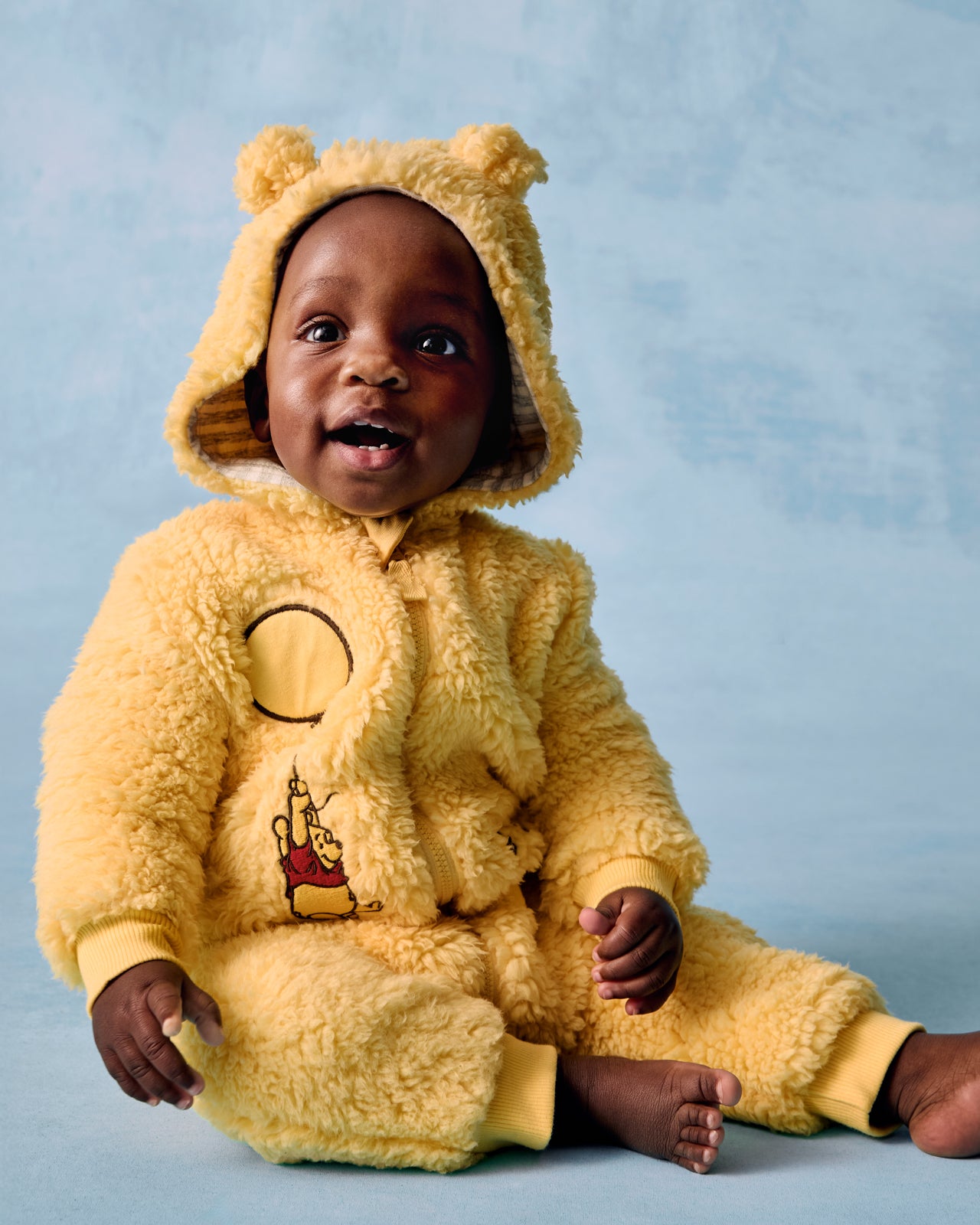 Sitting baby wearing the Disney Winnie the Pooh Sherpa Romper on a blue background