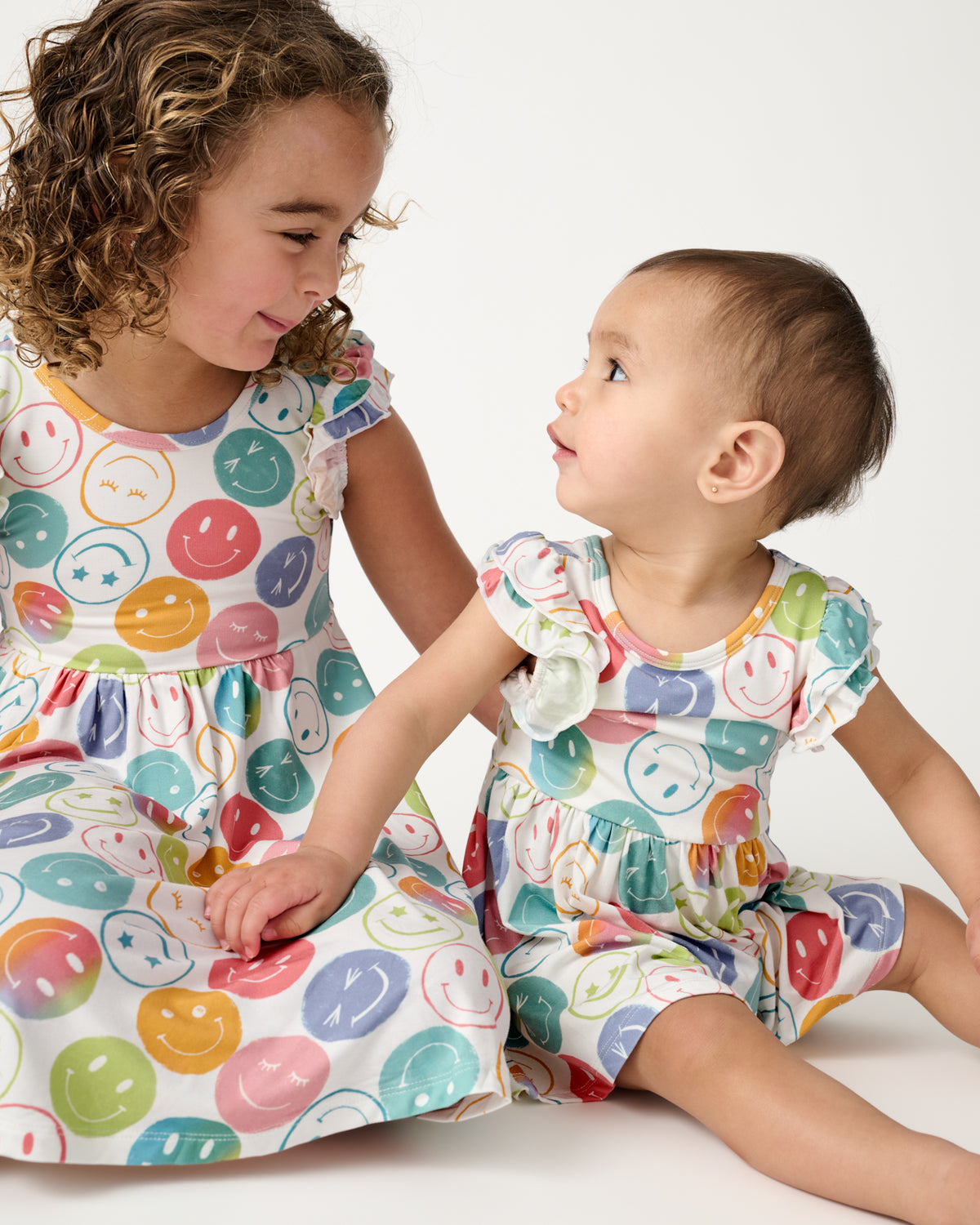 Two sitting children wearing matching Positive Vibes Flutter Twirl Dresses