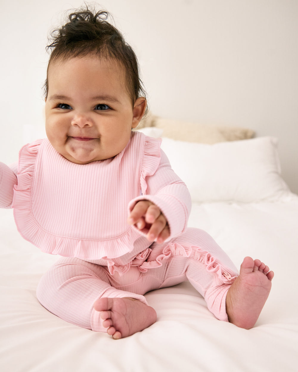 Newborn girl wearing the Prima Pink Ribbed Ruffle Bib with a matching pink zipper pajama