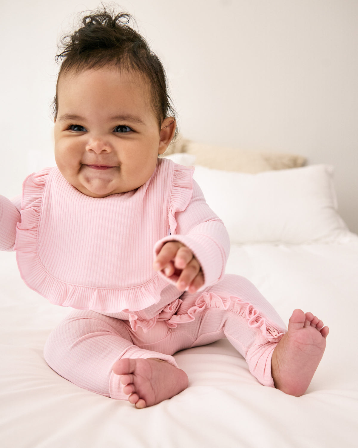 Newborn girl wearing the Prima Pink Ribbed Ruffle Bib with a matching pink zipper pajama