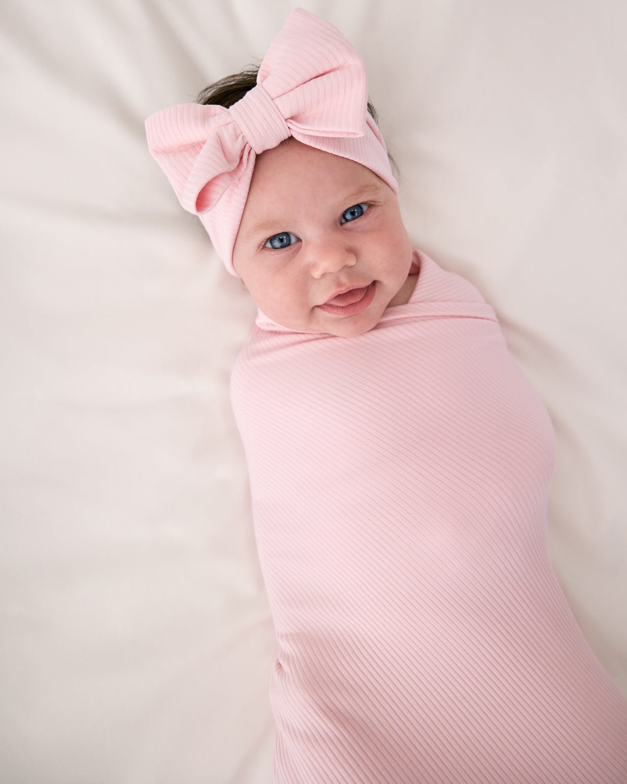 Close up of baby wearing the Prima Pink Ribbed Swaddle & Luxe Bow Headband Set