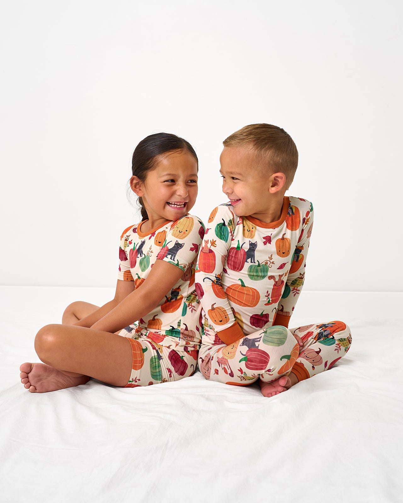Two children sitting back to back wearing Pumpkin Pals Two-Piece Pajama Sets
