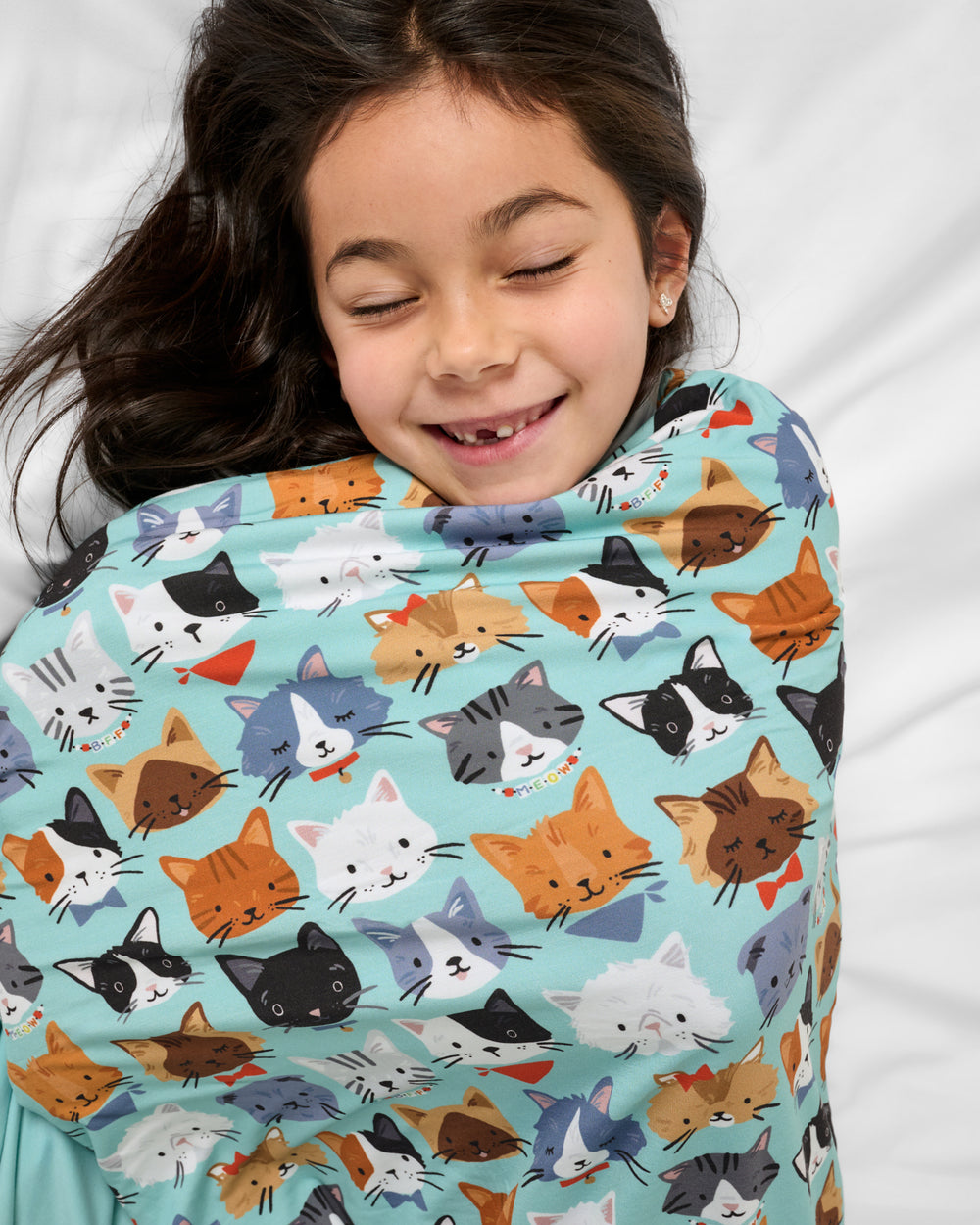 Girl wrapped in the Purrfect Pals Large Cloud Blanket® on a white bed