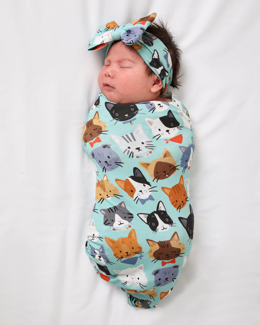 Aerial view of baby wearing the Purrfect Pals Swaddle & Luxe Bow Headband Set