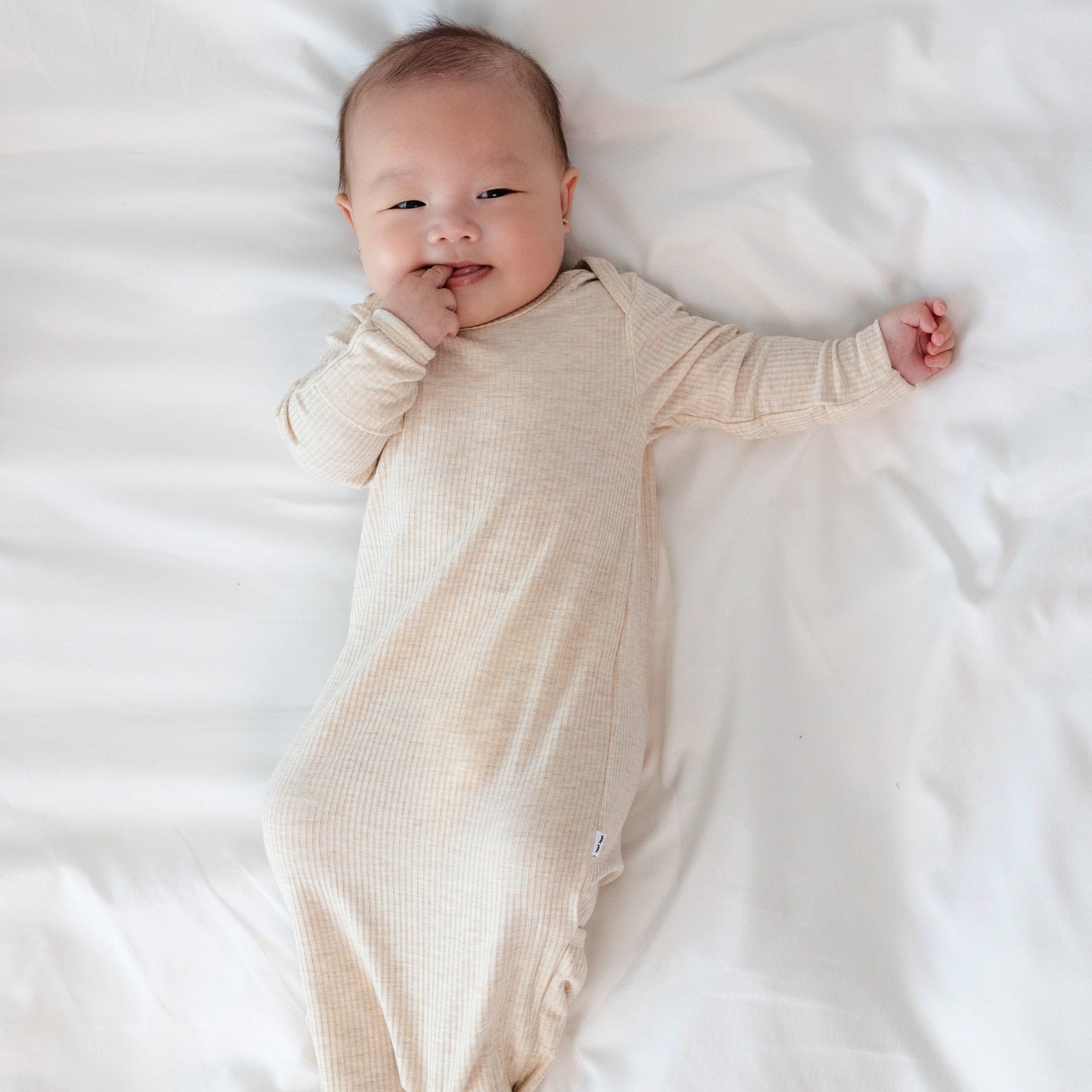 Closer up of Child laying on a bed wearing a Heather Oatmeal Ribbed Infant Gown