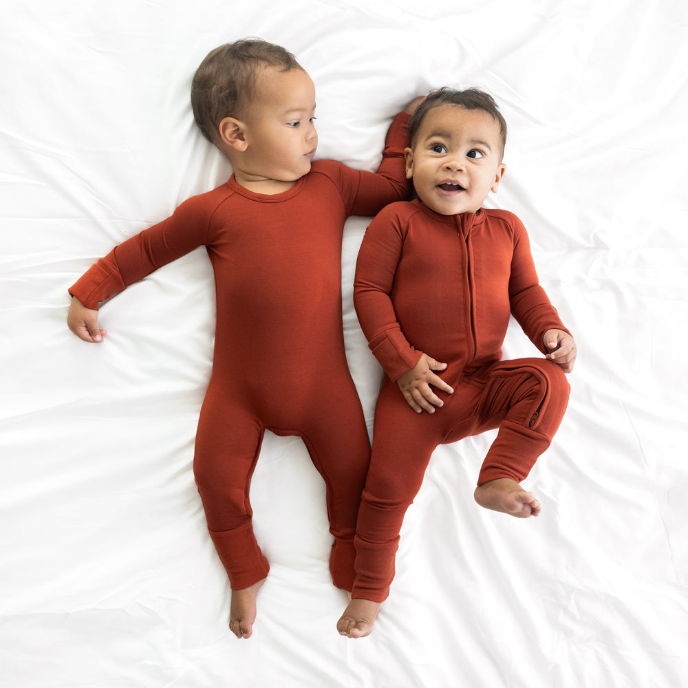 Two children laying on a bed wearing Cozy Rust zippies in crescent and standard styles