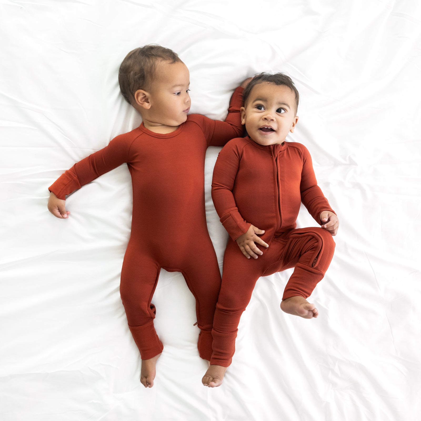 Two children laying on a bed wearing Cozy Rust zippies in crescent and standard styles