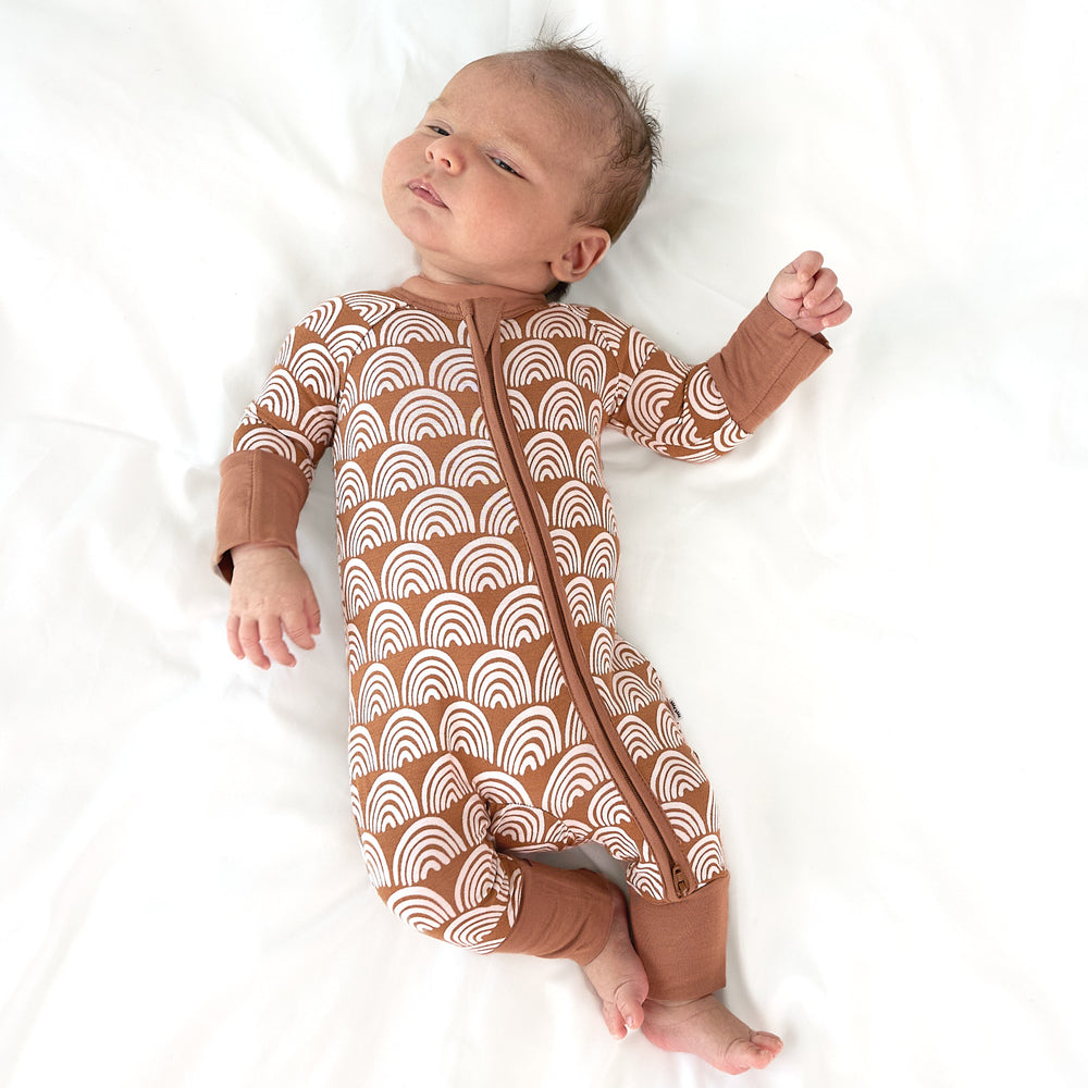 newborn baby laying on bed wearing rust rainbows zippy stretching