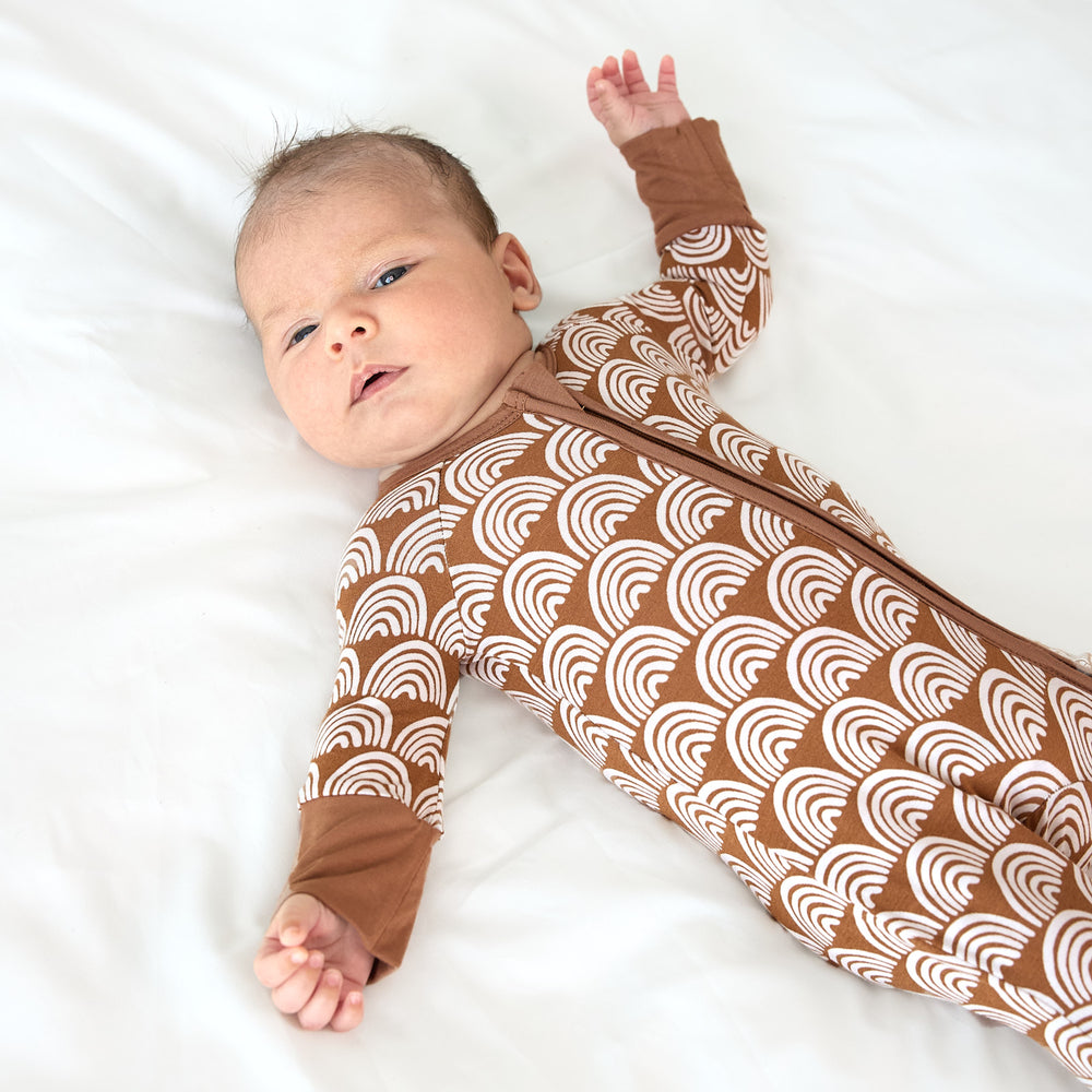 newborn baby laying on bed wearing rust rainbows zippy