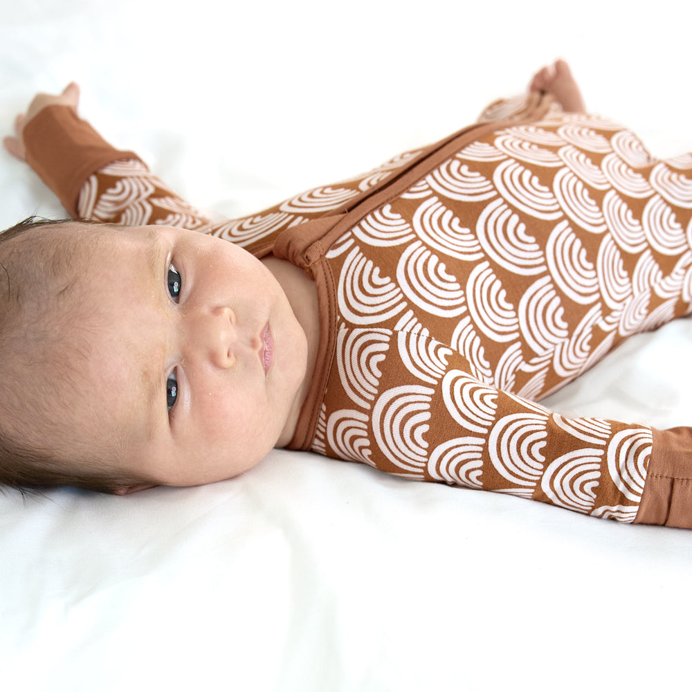 close up of newborn baby laying on bed wearing rust rainbows zippy