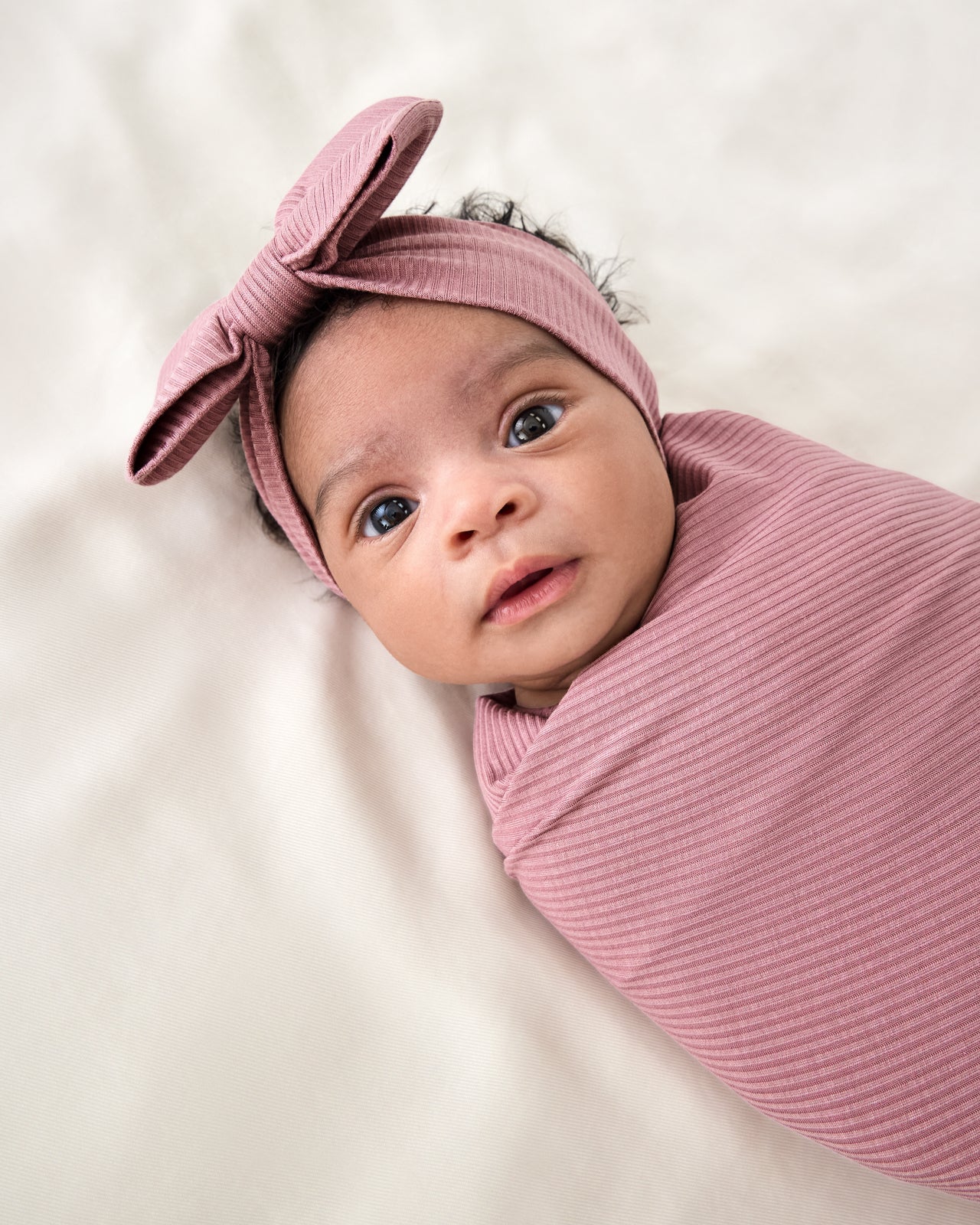Close up of baby wrapped in the Rosewood Ribbed Swaddle & Luxe Bow Headband Set