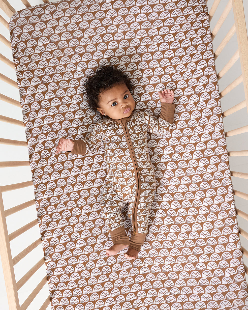Aerial view of baby laying on the Rust Rainbows Fitted Crib Sheet