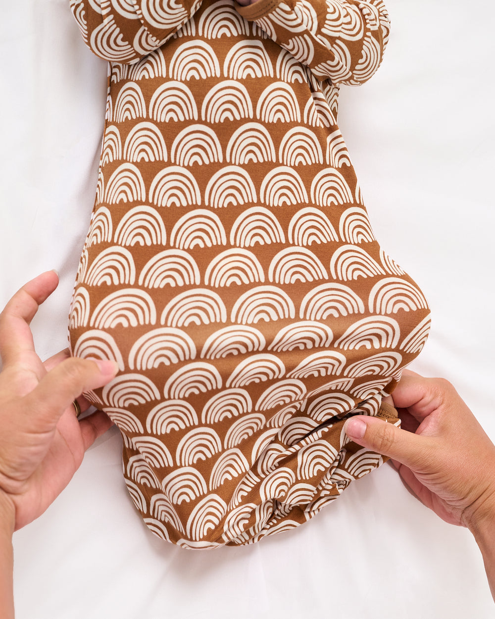 Adult adjusting the envelope sweep on the Rust Rainbows Infant Gown