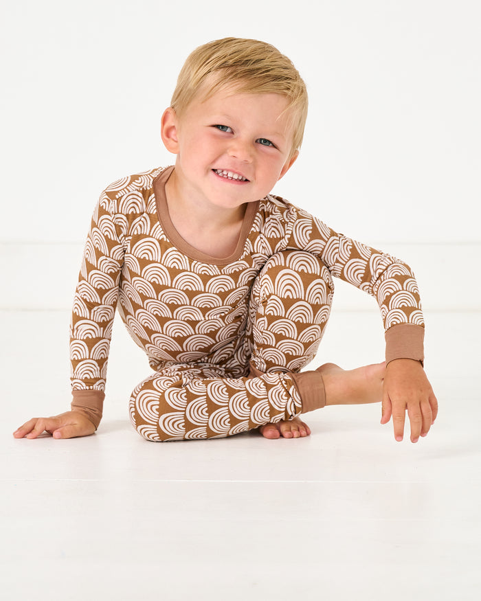 Sitting boy wearing the Rust Rainbows Two-Piece Pajama Set