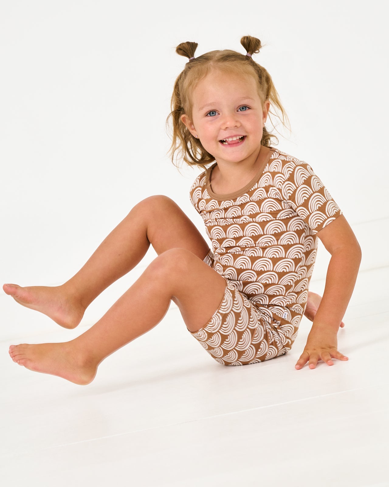 Sitting girl wearing the Rust Rainbows Two-Piece Short Sleeve & Shorts Pajama Set