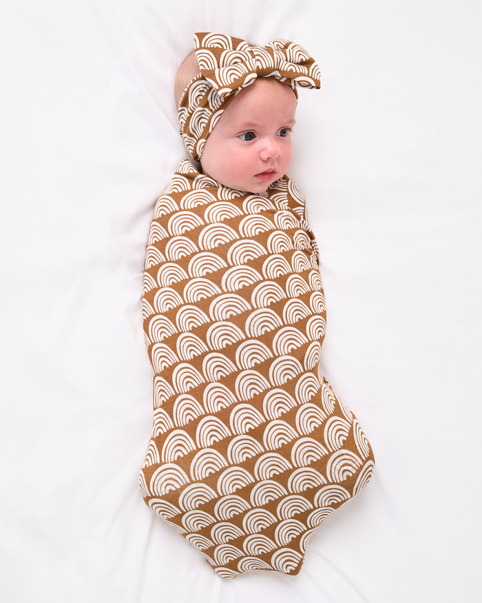 Aerial view of baby wearing the Rust Rainbows Swaddle & Luxe Bow Headband Set