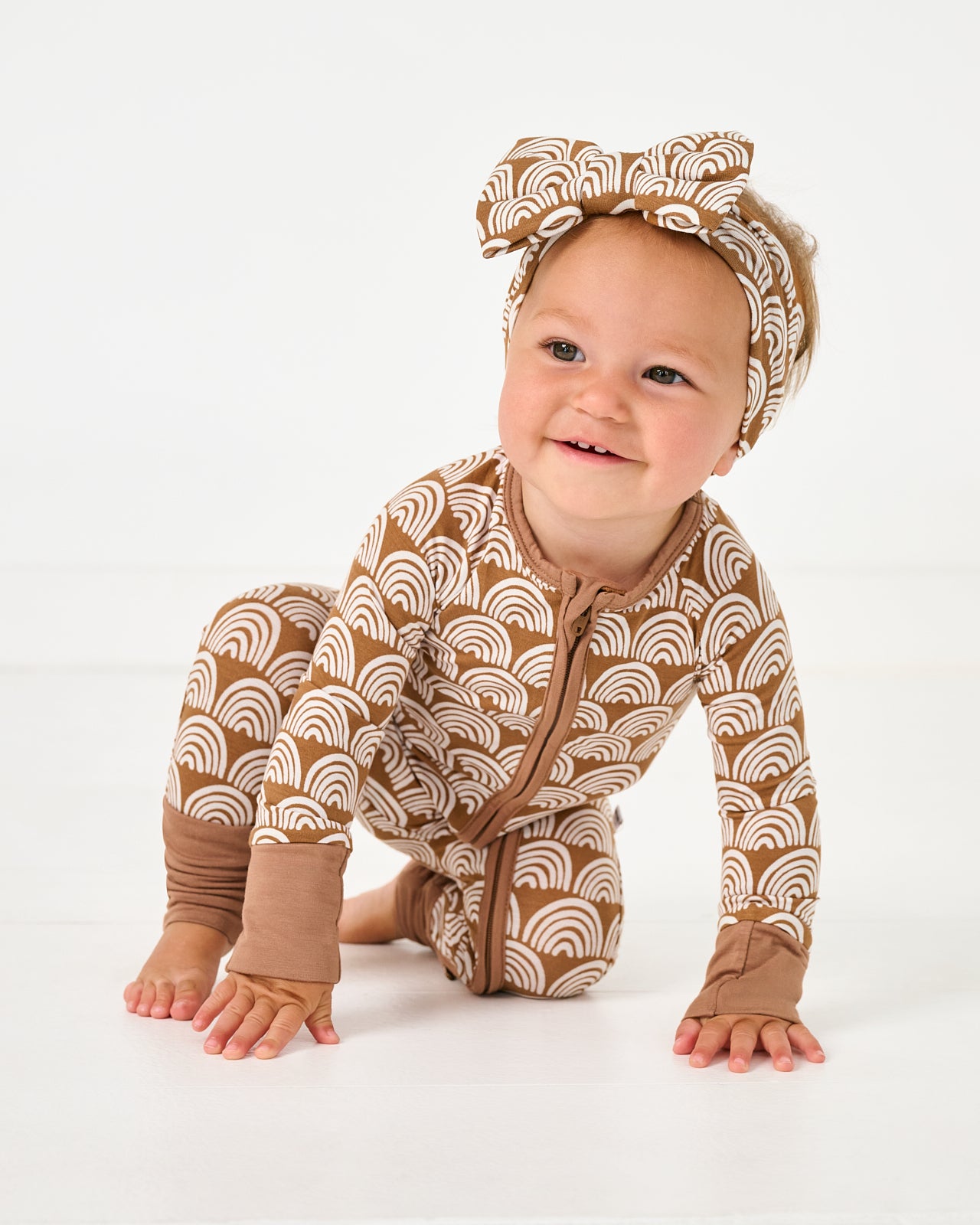 Crawling baby wearing the Rust Rainbows Zippy with a matching luxe bow headband