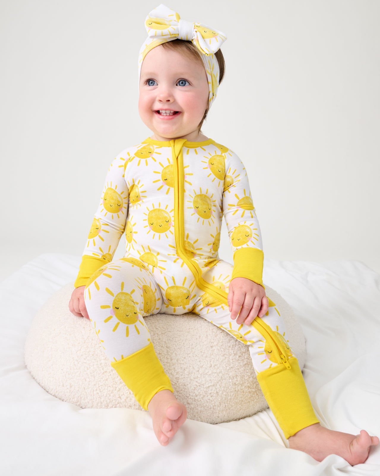 Baby sitting on a boucle ottoman wearing the Sunshine Zippy