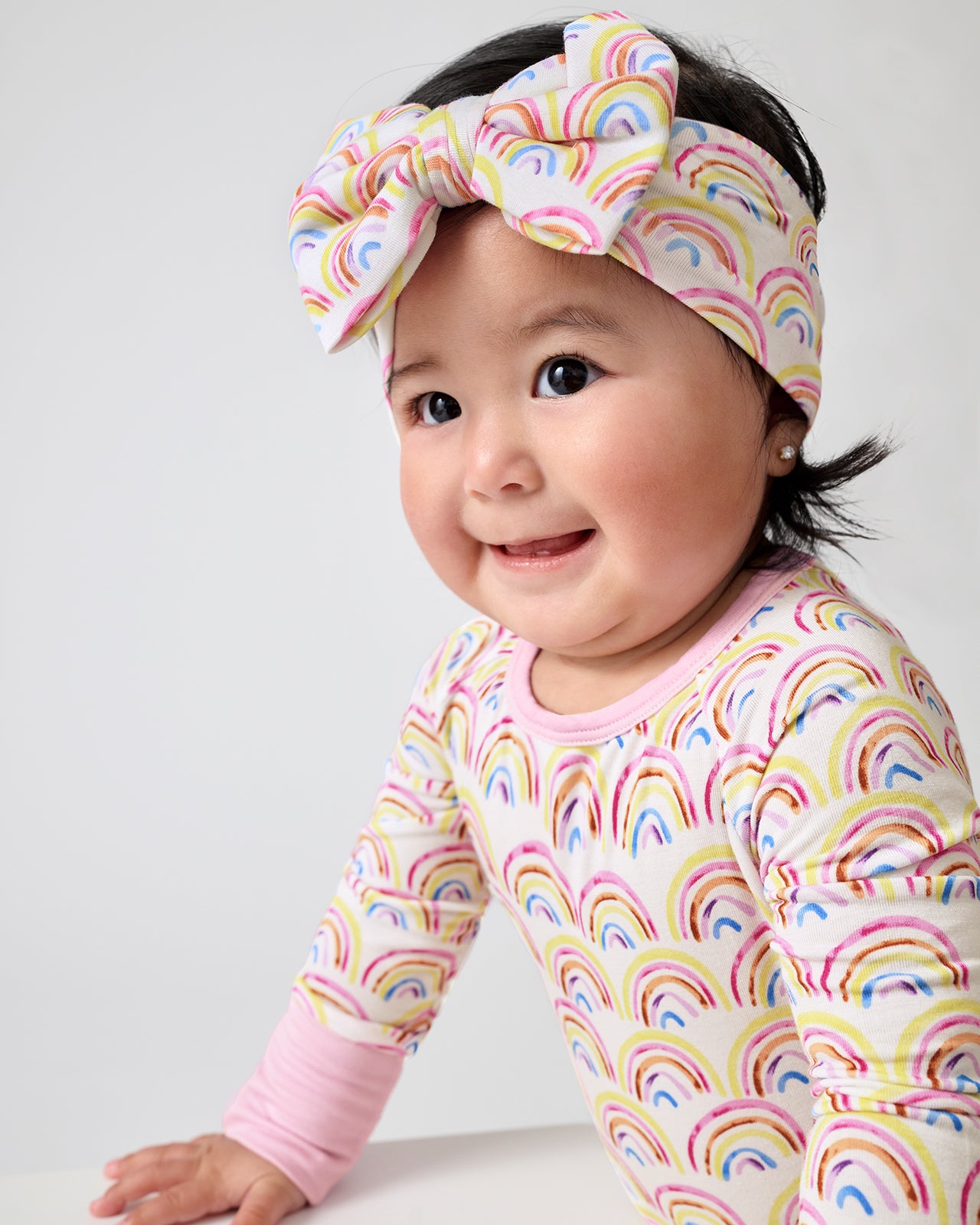 Baby wearing the Pastel Rainbows Luxe Bow Headband and Crescent Zippy