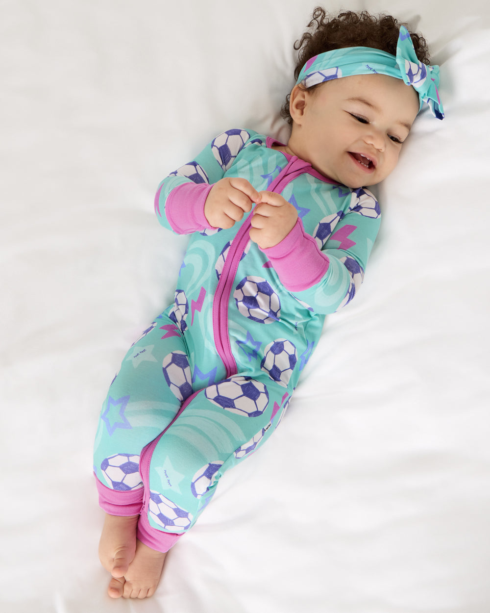 Aerial view of baby wearing the Aqua Soccer Stars Luxe Bow Headband and footie pajama