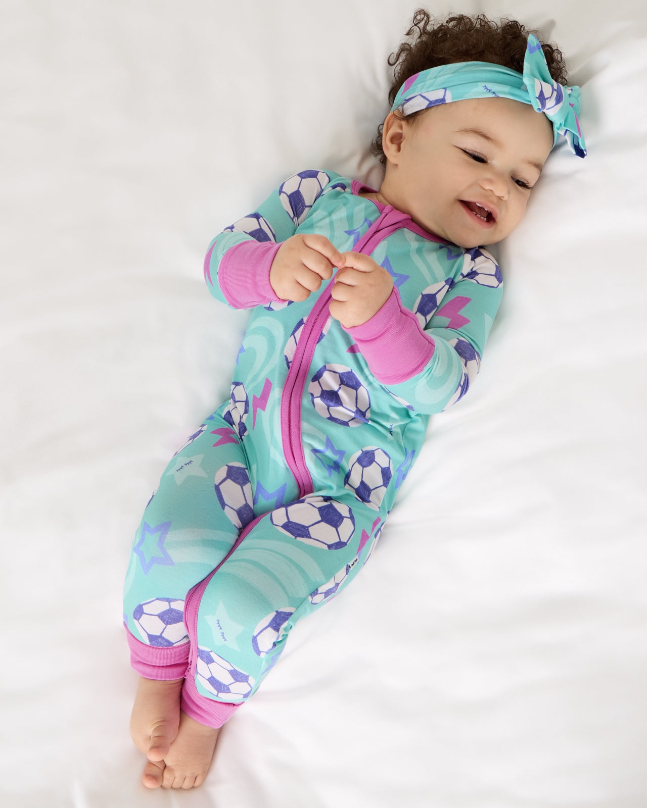 Aerial view of baby wearing the Aqua Soccer Stars Luxe Bow Headband and footie pajama