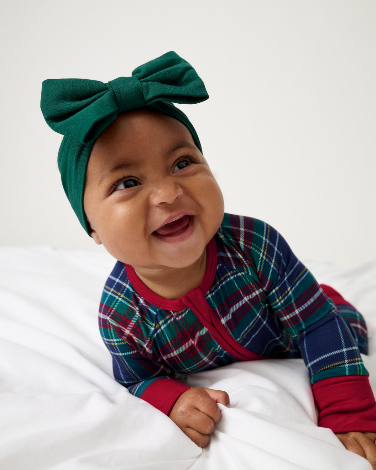 Baby wearing the Emerald Luxe Bow Headband and Northern Night Plaid Footie PJ